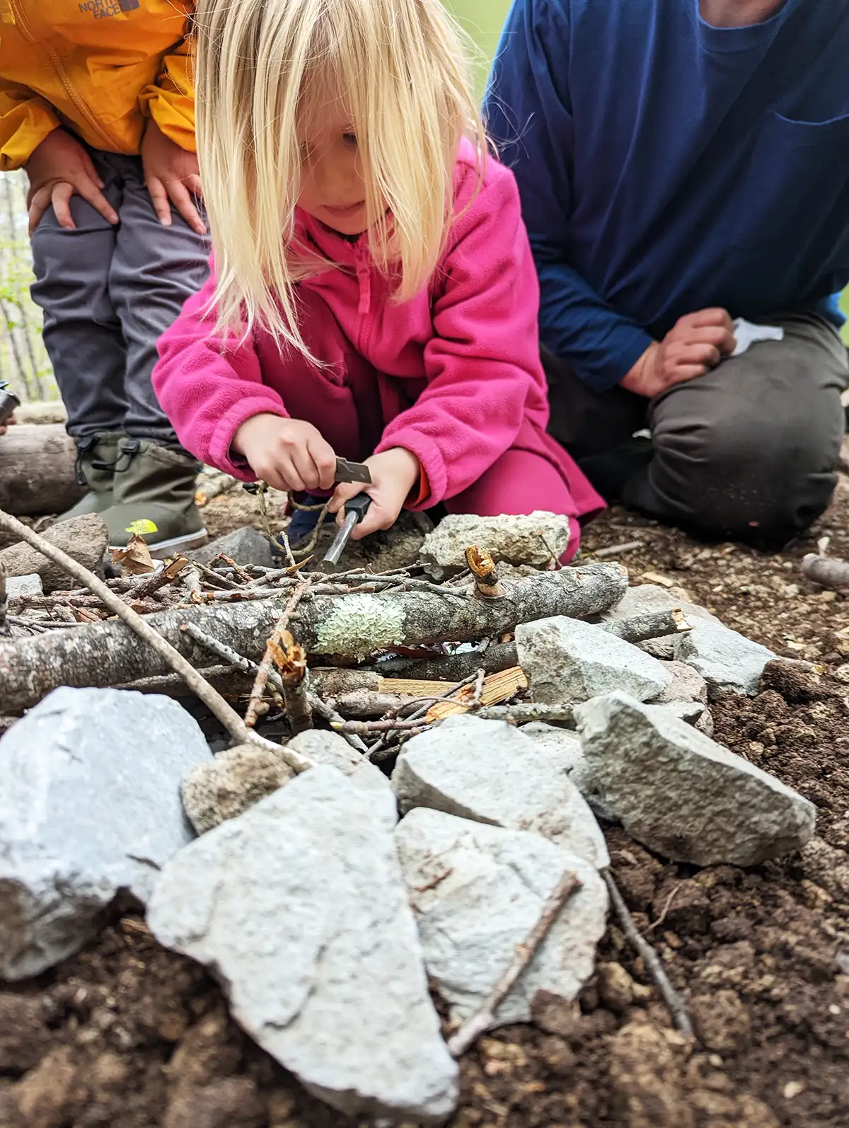 During TCG Summer Karuizawa Nature Adventure at Rising Field Karuizawa, a student eagerly tries using flint to make sparks for the campfire. With focused determination, she strikes the flint, aiming to ignite the fire. 