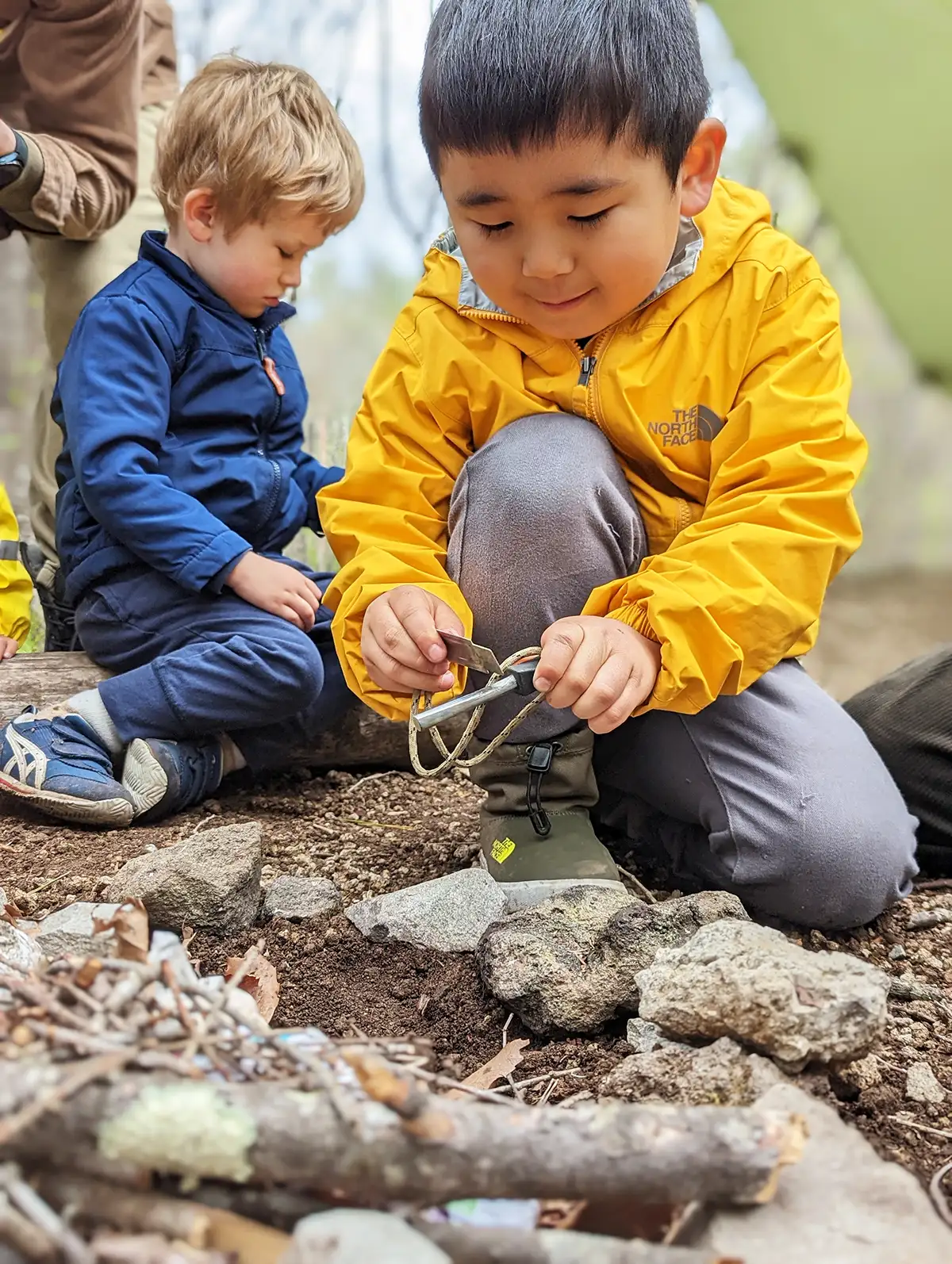 A TCG Summer Karuizawa Nature Adventure student at Rising Field focused on his task, determined to start the campfire. He struck the flint, igniting sparks. It was a hands-on learning moment in the picturesque setting of Karuizawa.